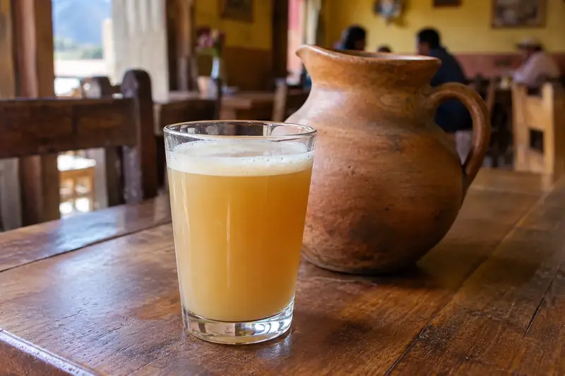 Verre de chicha de jora trouble et mousseuse, devant une cruche en terre cuite, dans une salle rustique