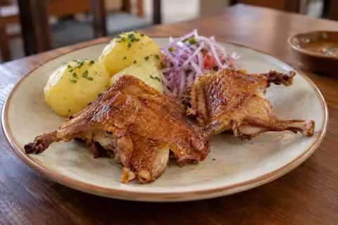 Deux morceaux de cuy frit à la peau dorée et croustillante, avec des pommes de terre et une salsa criolla