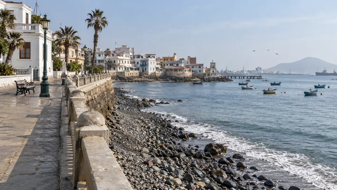 Promenade à balustrade au-dessus d’une plage de galets, bateaux de pêche au mouillage et port à l’horizon
