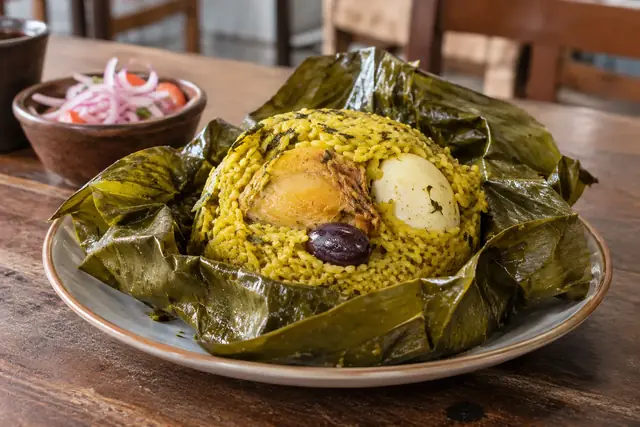 Juane ouvert dans sa feuille de bijao : riz jaune, morceau de poule, œuf et olive noire