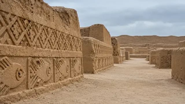 Murs d’adobe ornés de frises de poissons et de motifs géométriques en relief, le long d’une allée de terre