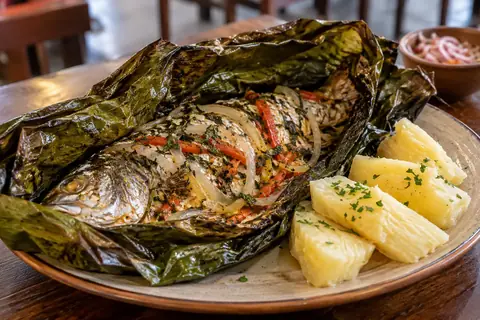 Poisson entier cuit dans des feuilles, avec oignon et poivron, servi avec des morceaux de manioc