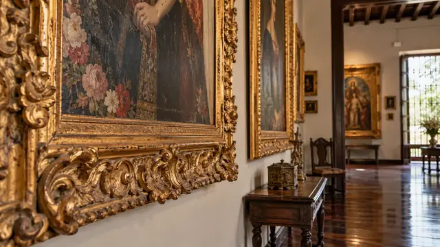 Salon d’une demeure ancienne : grands tableaux religieux dans des cadres dorés sculptés, parquet et mobilier de bois