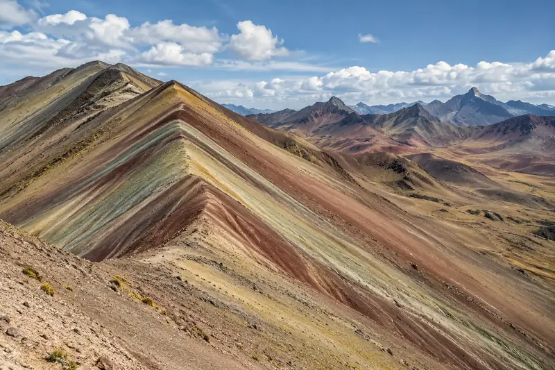 Crête de montagne rayée de bandes rouges, ocre et vertes, sous un ciel nuageux